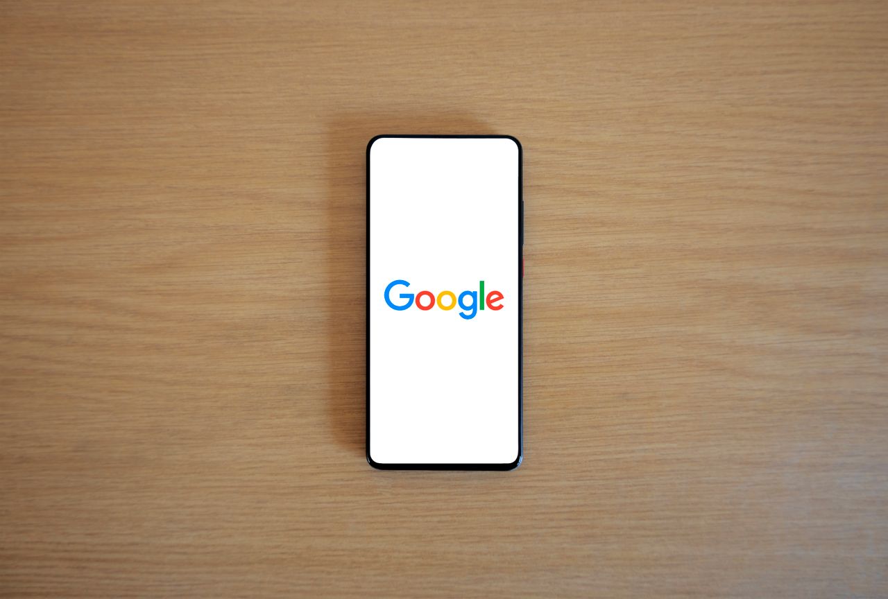 services-03 A smartphone displaying the Google homepage on a wooden surface, viewed from above.